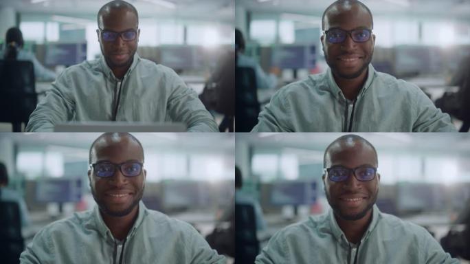 办公室: 专注的IT程序员的肖像戴着耳机在计算机上工作，看着相机并微笑着。黑人男性软件工程师开发创新