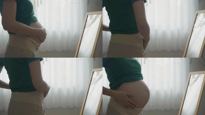 孕妇早上在镜子里欣赏肚子的特写镜头。