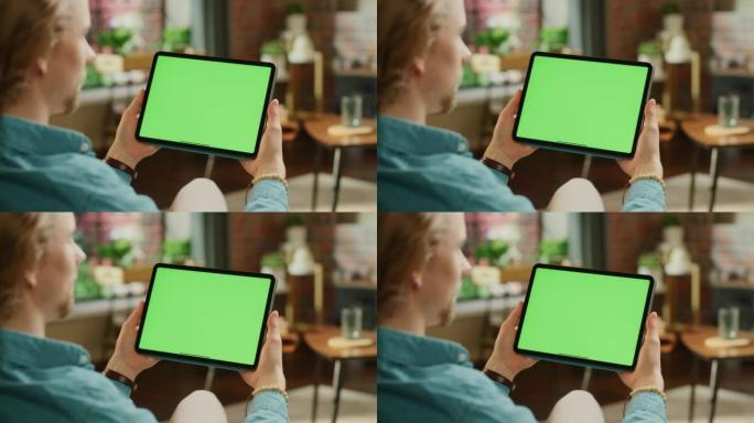 年轻人拿着平板电脑，绿屏模拟显示。男性在家放松，在移动设备上观看视频和阅读社交媒体帖子。特写镜头。