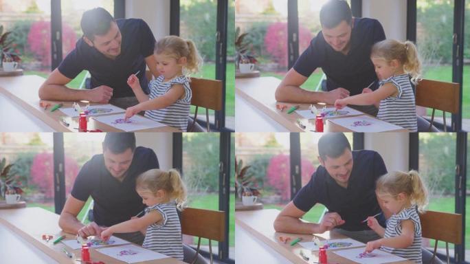 父亲和年幼的女儿一起在家里的桌子上做工艺和绘画装饰很开心