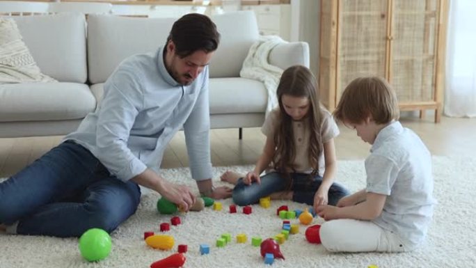 年轻的爸爸和可爱的小孩一起玩木制彩色积木
