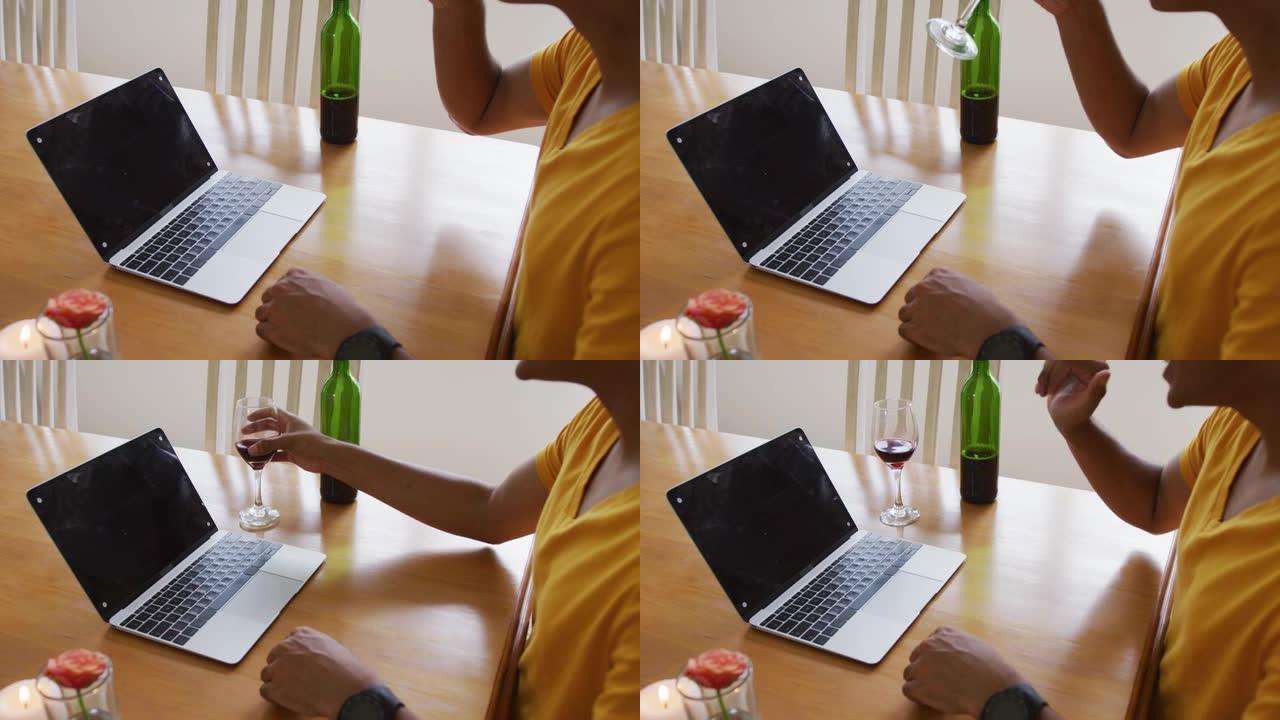 混合种族男子的中段坐在桌子旁，用笔记本电脑喝酒并挥舞着视频通话