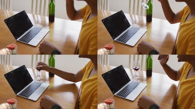 混合种族男子的中段坐在桌子旁，用笔记本电脑喝酒并挥舞着视频通话