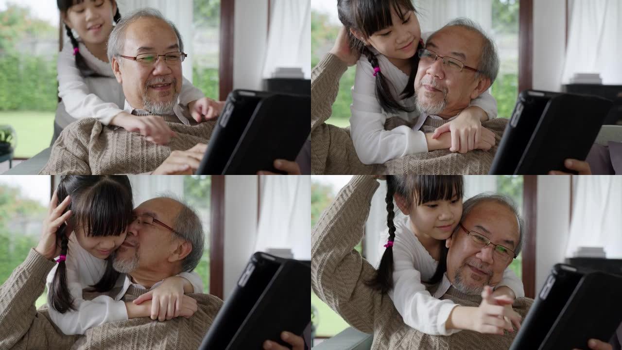 在家庭中的亲密关系中，与亚洲老前辈祖父母在家中与计算机平板电脑上的技术一起玩耍和观看。年轻女孩从后面
