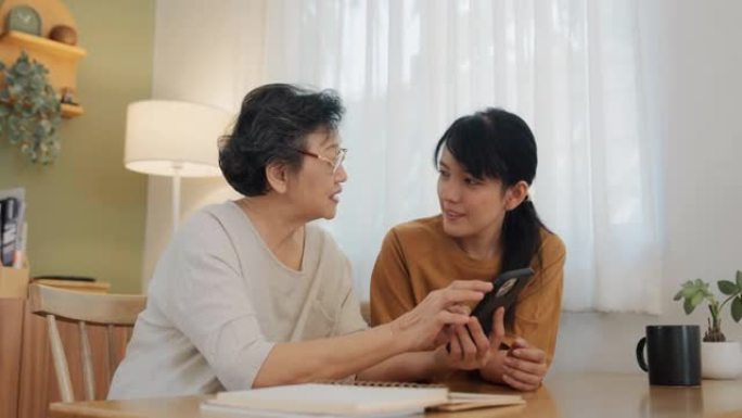 年轻的亚洲女性正在教她的母亲如何使用智能手机。