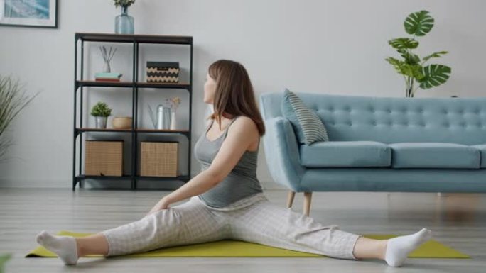 美丽的未来母亲伸展双腿独自坐在客厅的瑜伽垫上锻炼