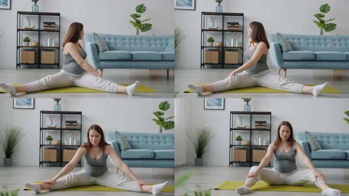 美丽的未来母亲伸展双腿独自坐在客厅的瑜伽垫上锻炼