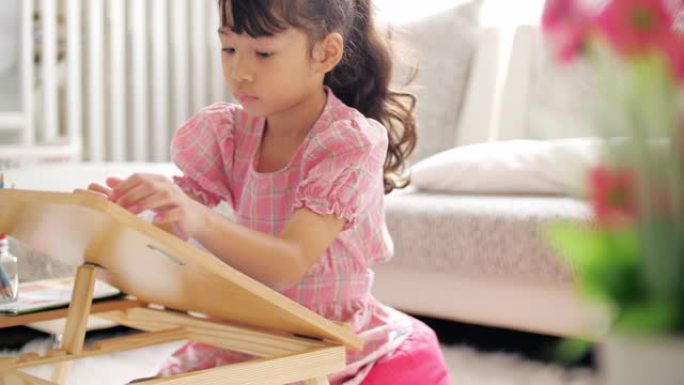 穿着粉色连衣裙的小女孩在家里的客厅画画和写字