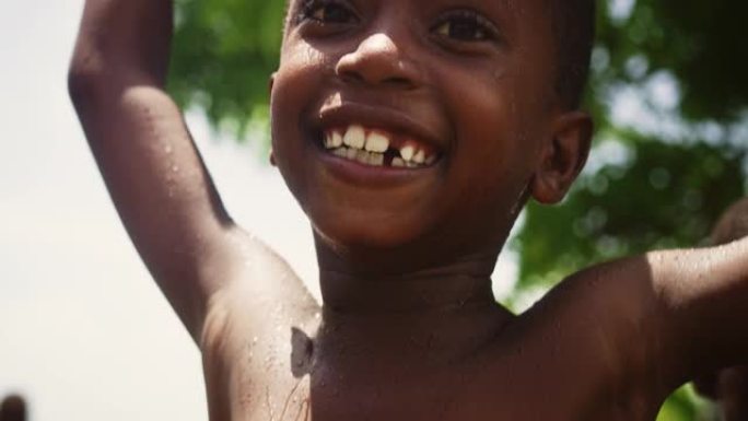 一个非洲小男孩在倒水下与其他孩子跳跃和跳舞的肖像。快乐天真的黑人儿童在久旱后玩耍享受雨水的祝福