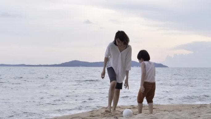 快乐快乐的亚洲母亲和5岁的儿子在日落时在海滩上踢足球。快乐的家庭在海滩上享受暑假。家庭时刻母亲和小男