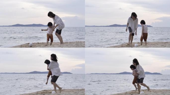 快乐快乐的亚洲母亲和5岁的儿子在日落时在海滩上踢足球。快乐的家庭在海滩上享受暑假。家庭时刻母亲和小男