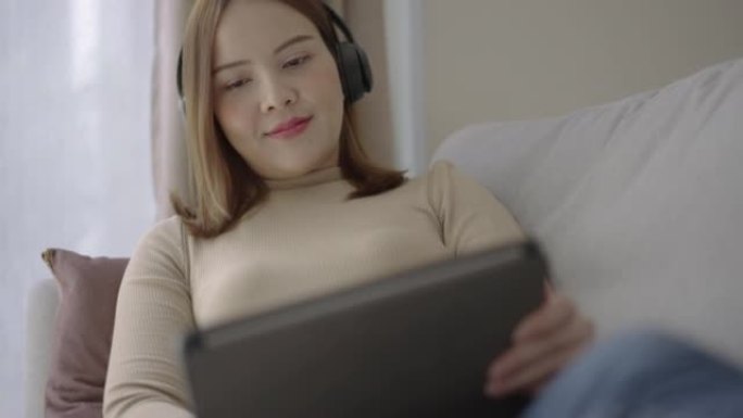 年轻的亚洲女性在家里放松时使用数字平板电脑听音乐