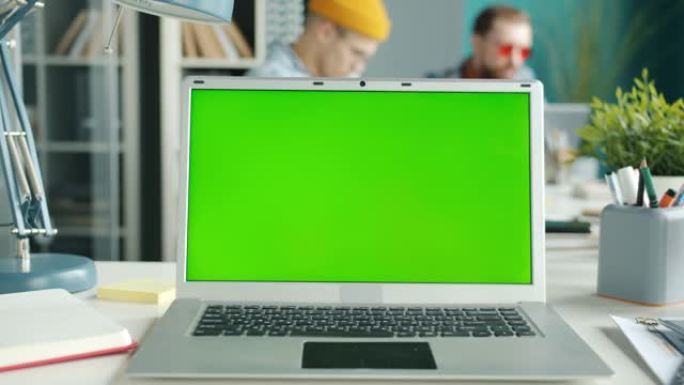 办公桌上的色度键绿屏笔记本电脑，员工在办公室背景中移动