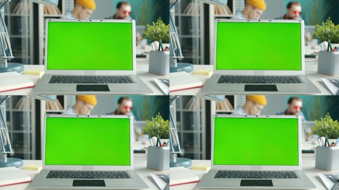 办公桌上的色度键绿屏笔记本电脑，员工在办公室背景中移动