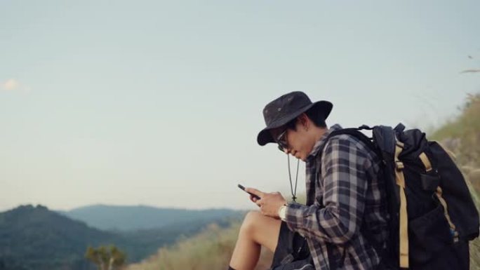 亚洲游客坐在岩石上，在山脉使用智能手机。