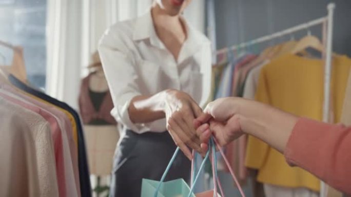 特写开朗的年轻亚洲女士购物新装礼品拿起购物袋后在布店购买布料和连衣裙。购物狂女孩，特价，活动生活理念