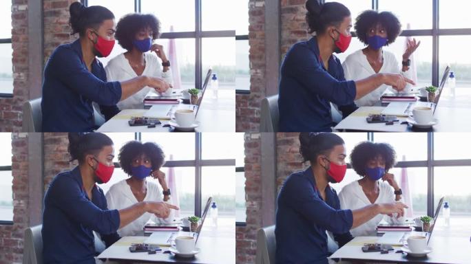 多元化的夫妇戴着口罩坐在咖啡馆里，使用笔记本电脑聊天