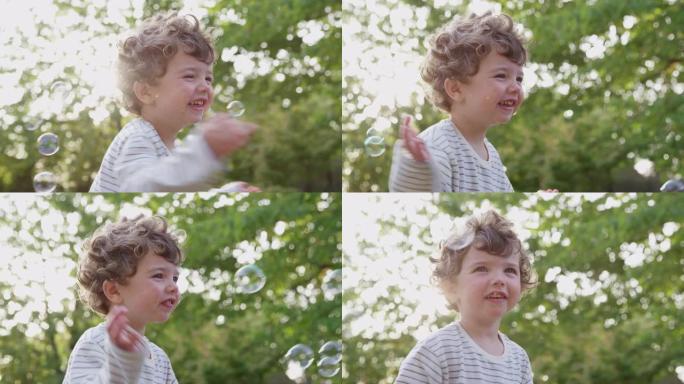 小男孩在花园追逐和破裂泡沫中玩耍
