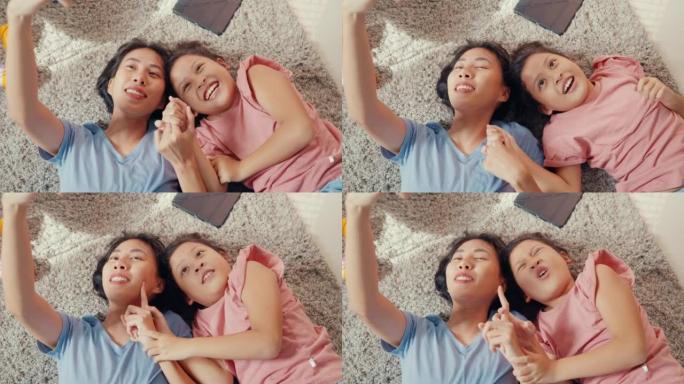 亚洲蹒跚学步的小女孩女儿与母亲使用智能手机在地毯地板上拍照或视频通话，在家里的客厅开心，开心。