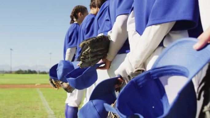 手持头盔和手套站在场上的女棒球运动员队伍的中部