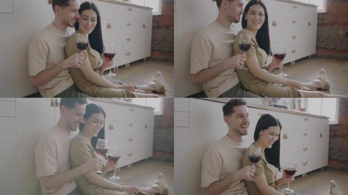 快乐的男人和女人碰碰酒杯，一起坐在厨房地板上敬酒和大笑