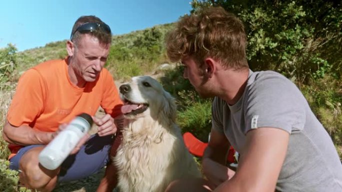特写视频，父亲和成年儿子在爬山休息时给狗喝水