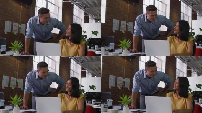 在工作中讨论的男女同事看着笔记本电脑并微笑着