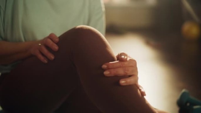 一名老年妇女在早上锻炼时感到膝盖疼痛不舒服，同时在家中的瑜伽垫上锻炼。中年女性按摩腿部以减轻疼痛。