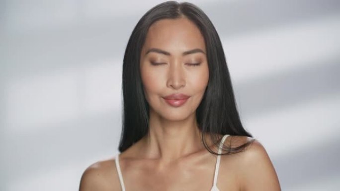 女性美女肖像。美丽多样的亚洲黑发女人摆姿势，微笑着，用自然健康的皮肤触摸她的脸。柔软孤立背景下的健康