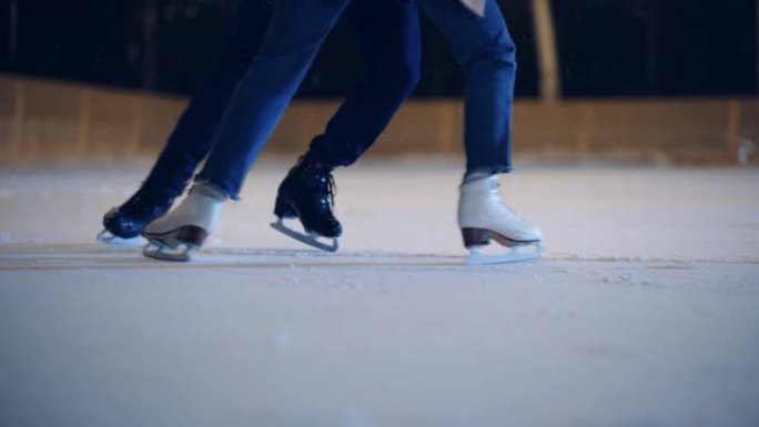 浪漫的冬天下雪的夜晚: 滑冰夫妇在溜冰场上玩得开心。户外双人滑冰。男女朋友培训。专注于腿和冰鞋