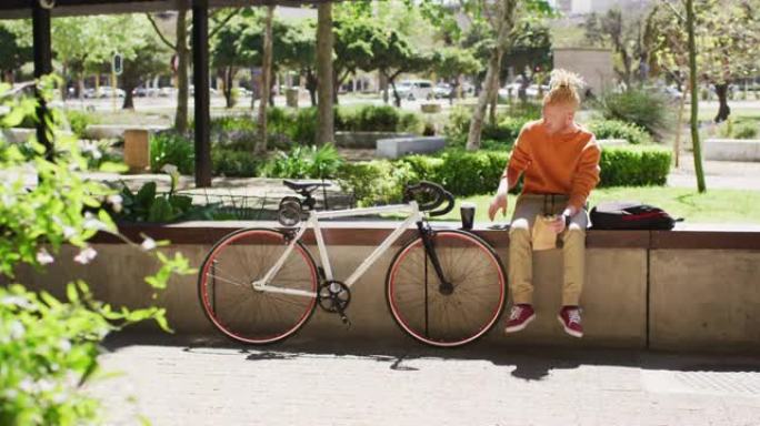 体贴的白化病非裔美国男子，长发lock坐在公园里，用智能手机骑自行车