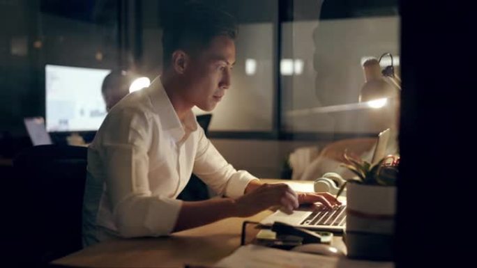 亚洲商人，晚上在办公室从事营销或广告工作的笔记本电脑和电话。在工作场所的计算机检查电子邮件，网络或在