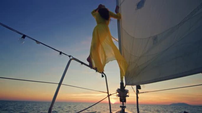 穿着黄色长裙的SLO MO女人在日落时享受帆船船头的微风