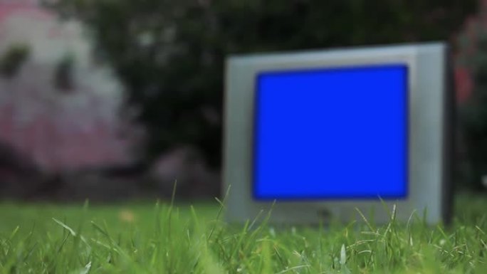 绿色草地上蓝屏的旧模糊电视。