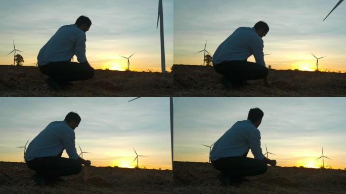 年轻的男性工程师在风力发电站工作时，用土壤检查风向的轮廓日落的后视图，检查风车农场的能源生产。可再生