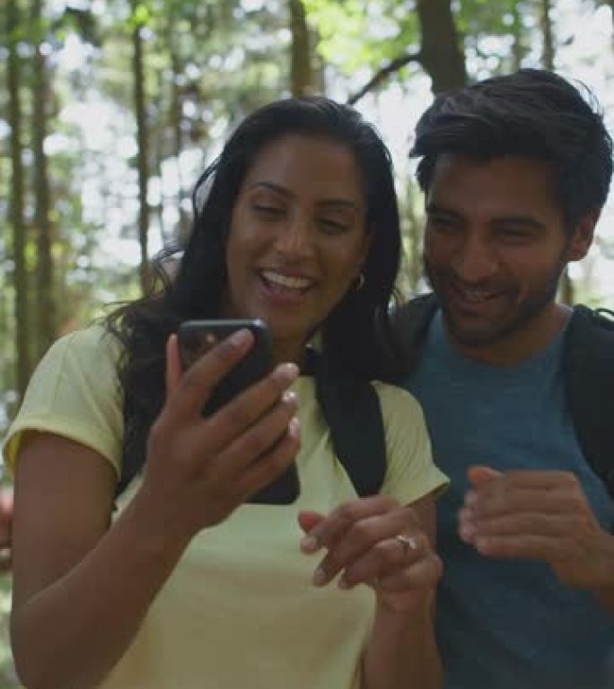 情侣用手机自拍徒步旅行或漫步夏日林地乡村的垂直视频