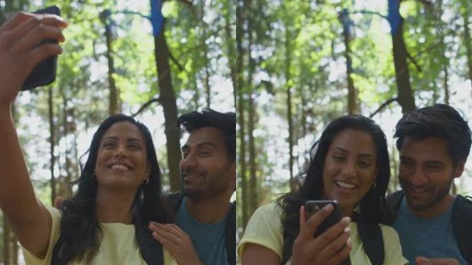情侣用手机自拍徒步旅行或漫步夏日林地乡村的垂直视频