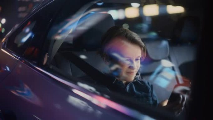 小男孩坐在汽车后座上，晚上通勤回家。乘客在带有工作霓虹灯的城市街道上乘坐出租车时，在智能手机上观看有