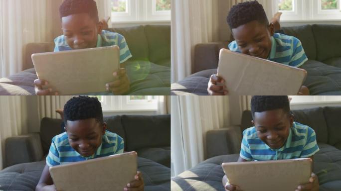 快乐的非洲裔美国男孩躺在沙发上，用平板电脑微笑