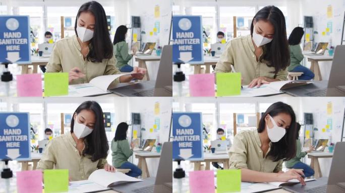 亚洲女商人企业家戴着医用口罩，在新的正常情况下保持社交距离，以预防病毒，同时在办公室工作时使用笔记本