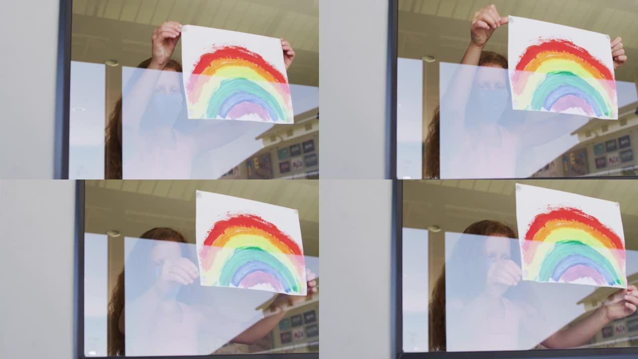 戴口罩的女孩在学校将彩虹画贴在窗户上