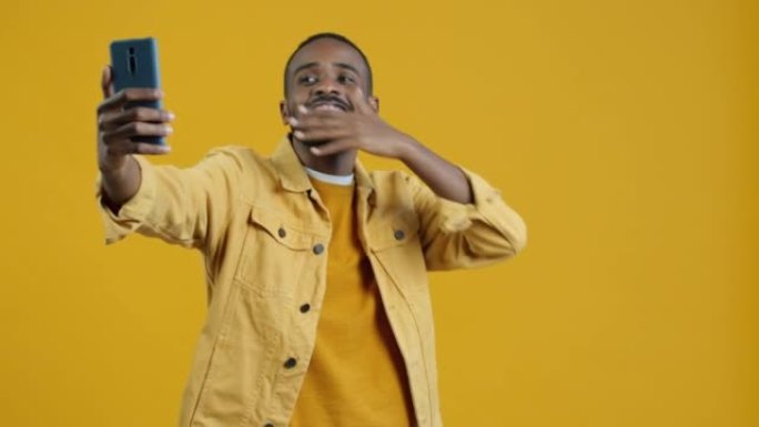 在黄色背景上使用智能手机进行视频通话时，快乐的非洲裔美国人男子的肖像