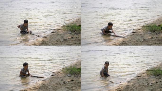 快乐男孩坐在湖岸独自玩木棍。