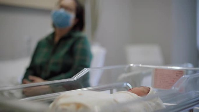 母亲戴着防病毒口罩在医院欣赏熟睡的新生儿