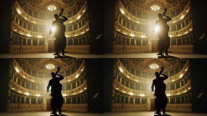 男性大提琴家的电影剪影正在经典的剧院舞台上演奏大提琴，并带有戏剧性的灯光