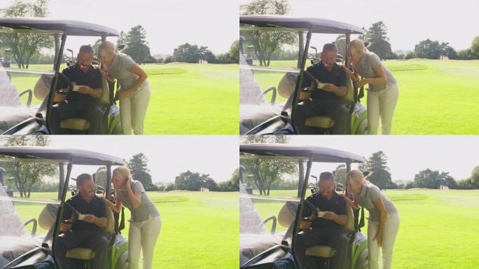 成熟的夫妇一起坐在计分卡的马车里打高尔夫球