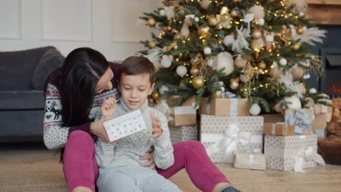 有爱心的妈妈给快乐的儿子送礼品盒，孩子拆包礼物送圣诞节智能手机