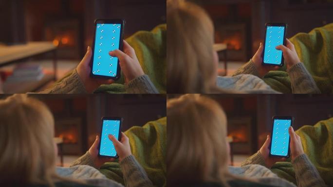 在家中的女人躺在休息室的沙发上，用蓝屏手机用舒适的火