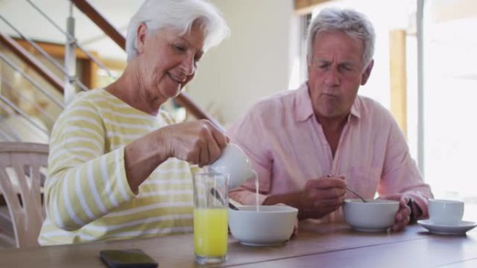 白人高级夫妇在谷物碗里倒牛奶，在家一起吃早餐