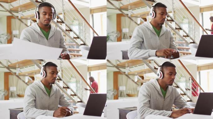 非洲裔美国十几岁的儿子戴着耳机，使用父亲背景的笔记本电脑